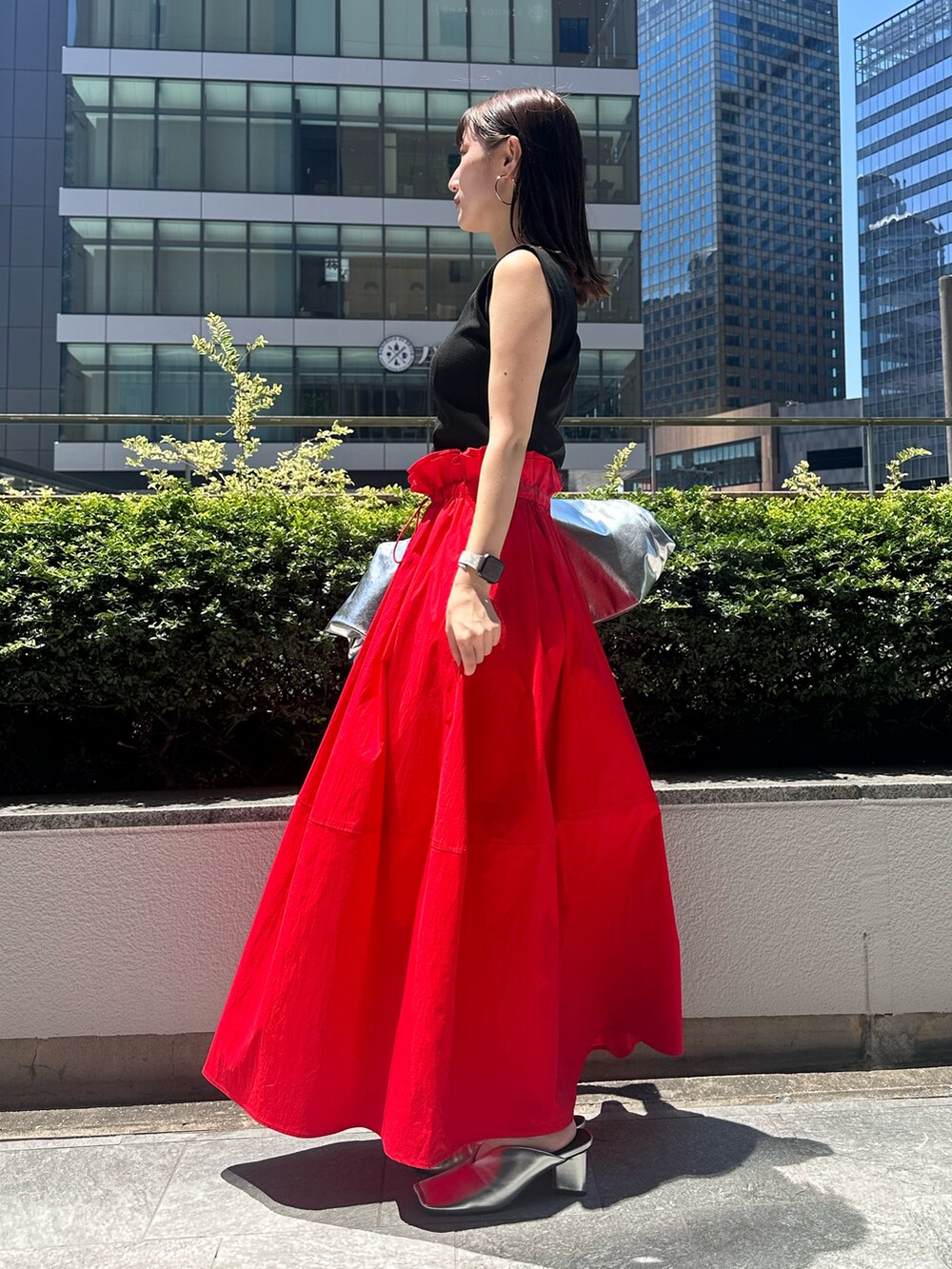 レッド系のスカート、シルバー系のトートバッグ、シルバー系のパンプスを着用したレディースの夏コーディネートの2枚目の写真