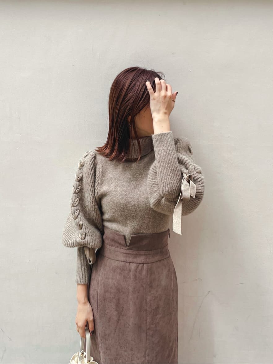 ブラック系のブーツ、ブラウン系のスカート、ベージュ系のニット/セーターを着用したレディースの秋コーディネートの2枚目の写真