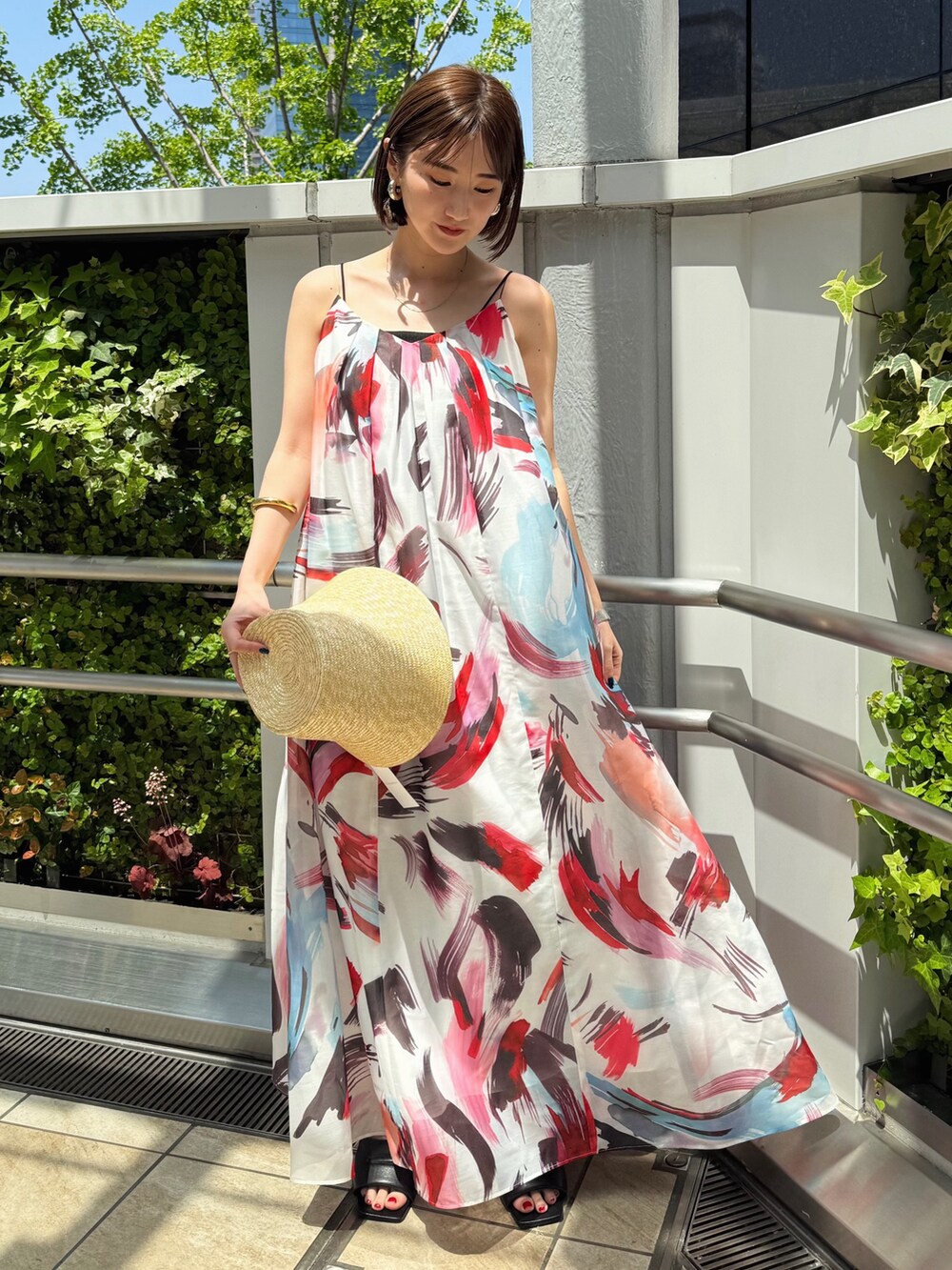 レッド系のワンピース、ブラック系のサンダル、ベージュ系のハットを着用したレディースの春コーディネートの2枚目の写真