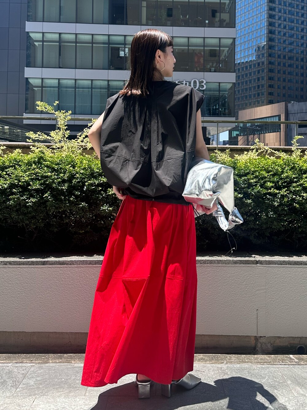 レッド系のスカート、シルバー系のパンプス、シルバー系のトートバッグを着用したレディースの夏コーディネートの4枚目の写真