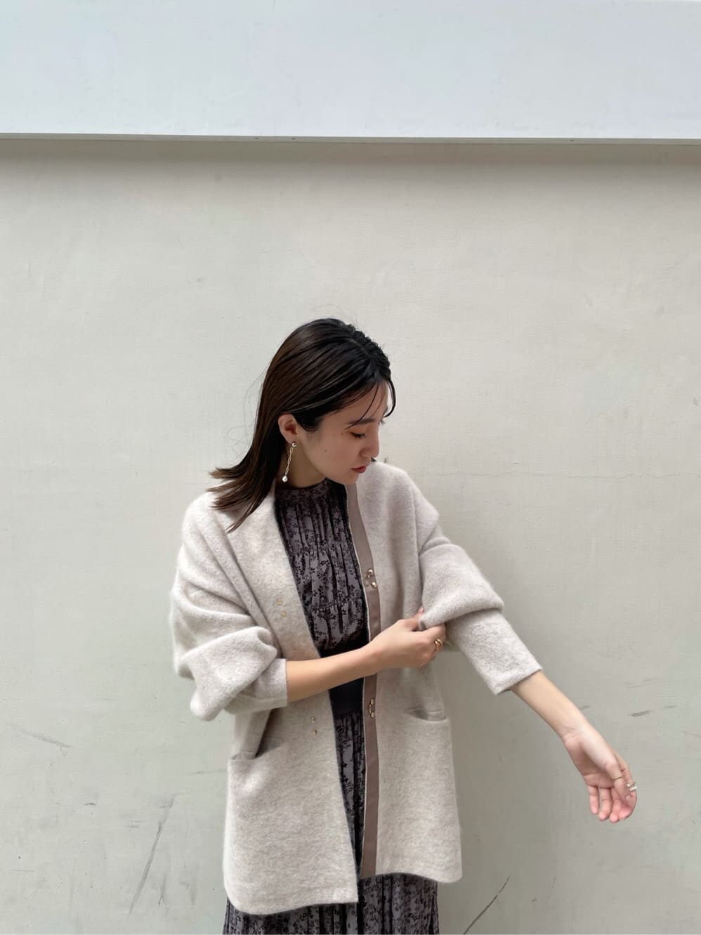 グレー系のワンピース、ホワイト系のカーディガン/ボレロ、ホワイト系のピアス（両耳用）を着用したレディースの秋コーディネートの3枚目の写真