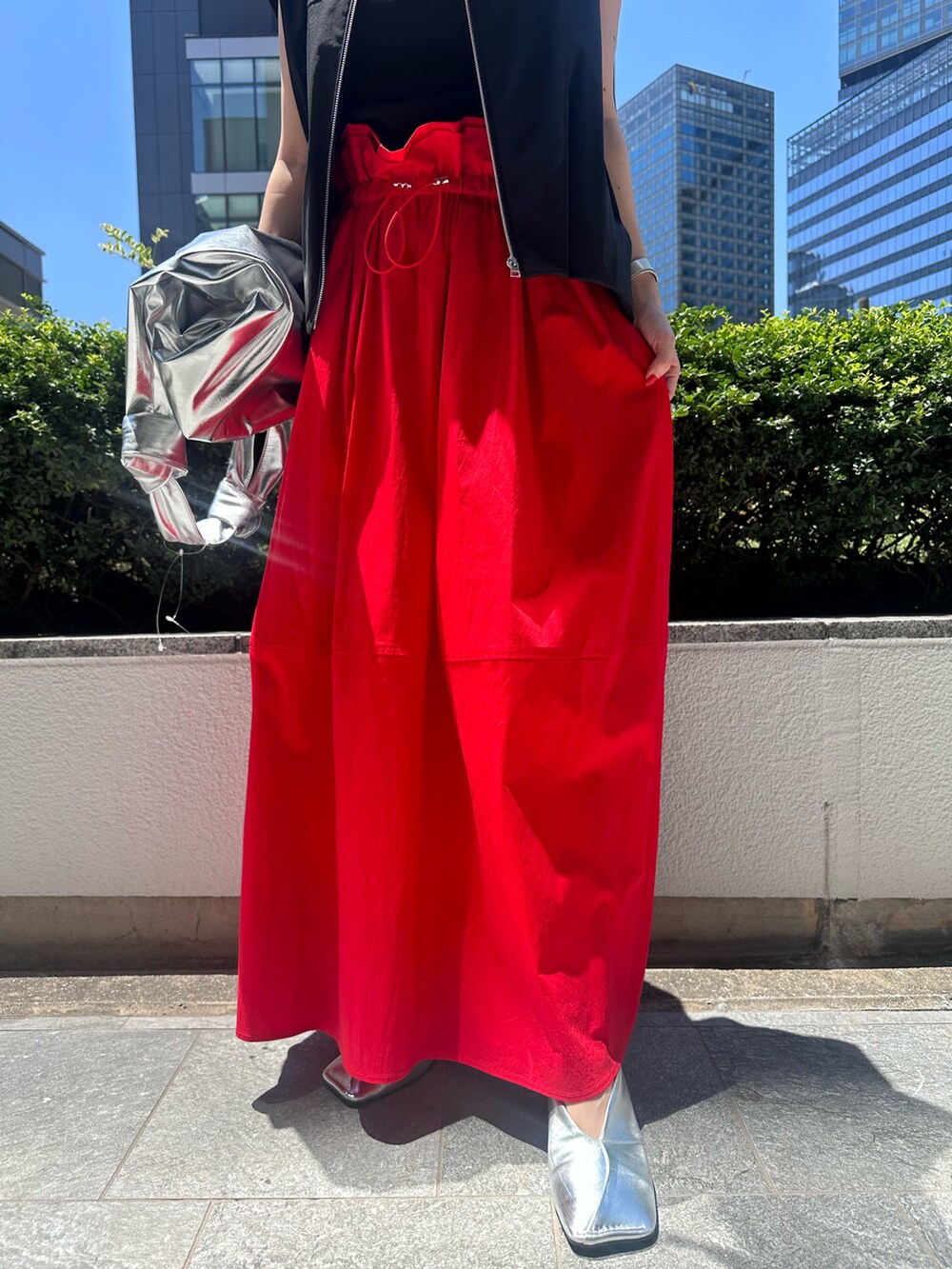 レッド系のスカート、シルバー系のトートバッグ、シルバー系のパンプスを着用したレディースの夏コーディネートの6枚目の写真