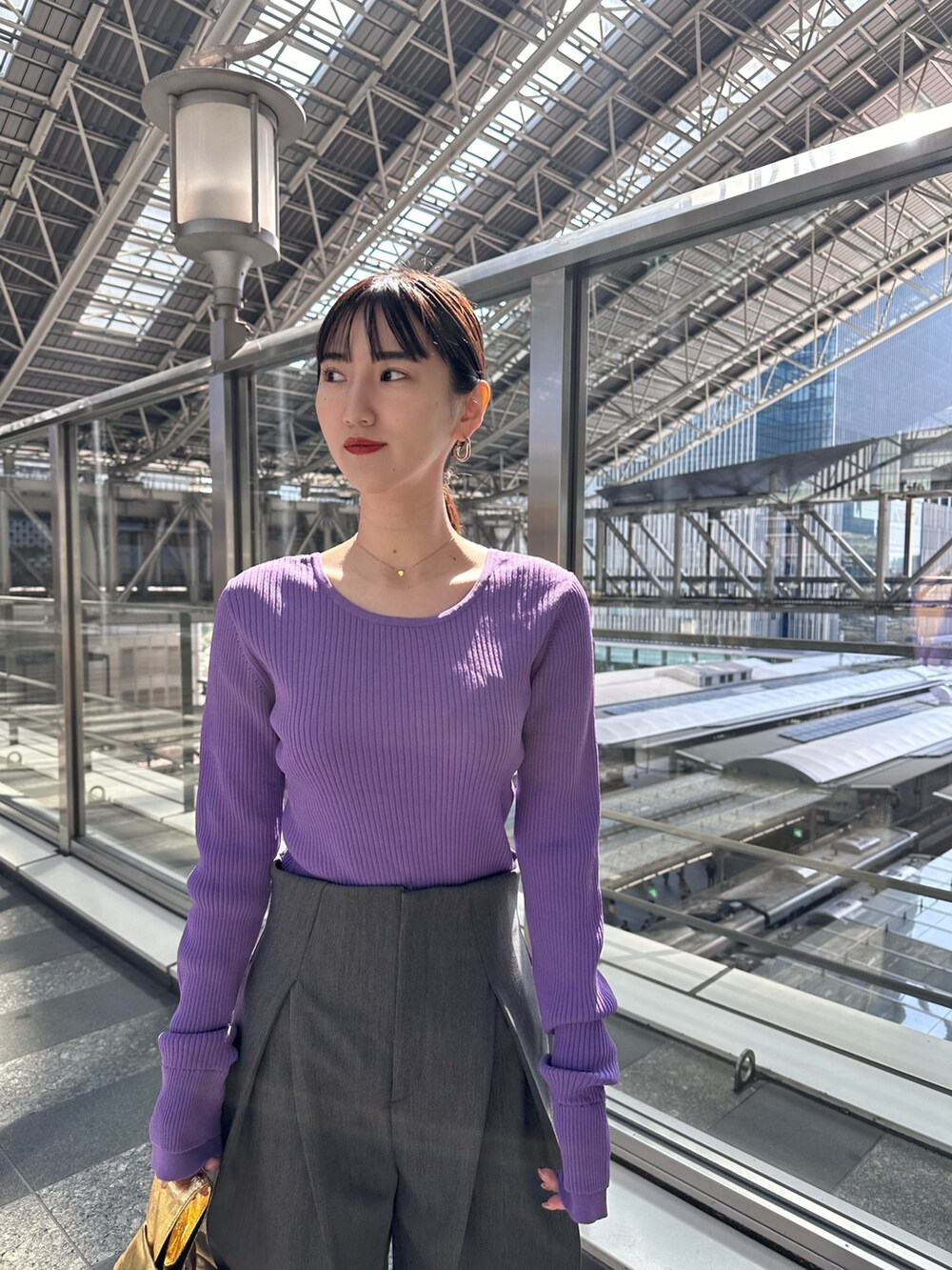 パープル系のニット/セーター、グレー系のその他パンツ、ゴールド系のハンドバッグを着用したレディースの春コーディネートの2枚目の写真