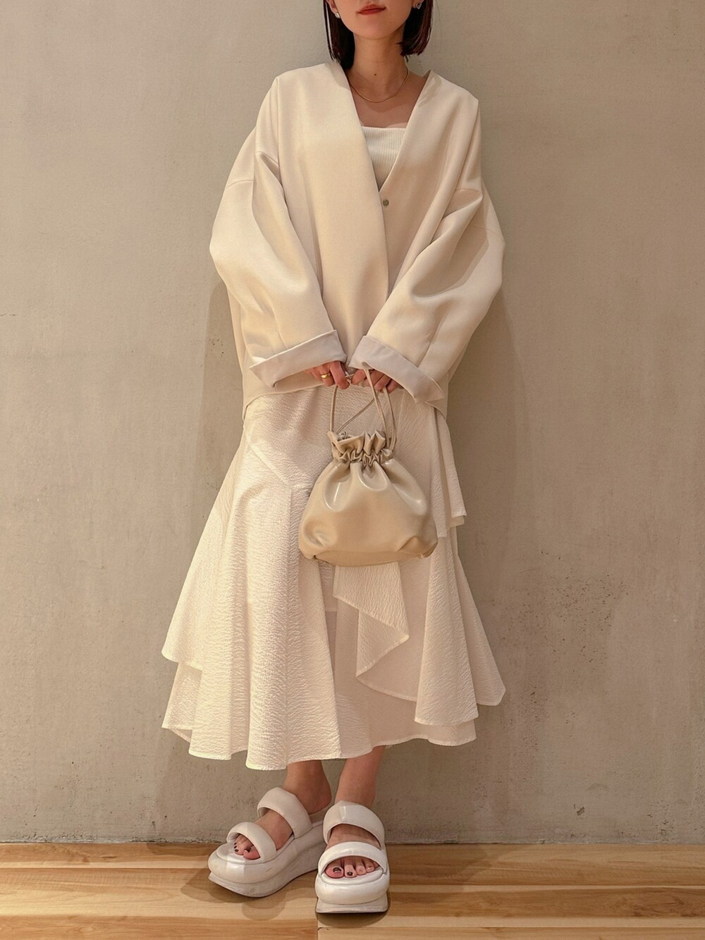 ブラウン系のノーカラーコート、ホワイト系のスカート、ホワイト系のサンダルを着用したレディースの春コーディネートの2枚目の写真