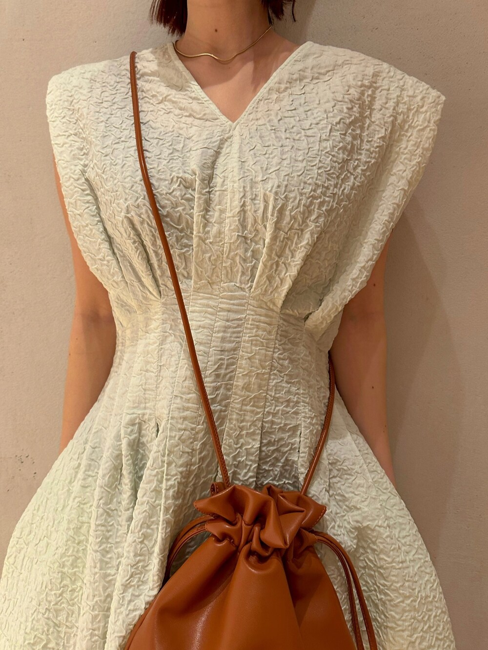 ベージュ系のテーラードジャケット、グリーン系のワンピース、ホワイト系のサンダルを着用したレディースの冬コーディネートの3枚目の写真