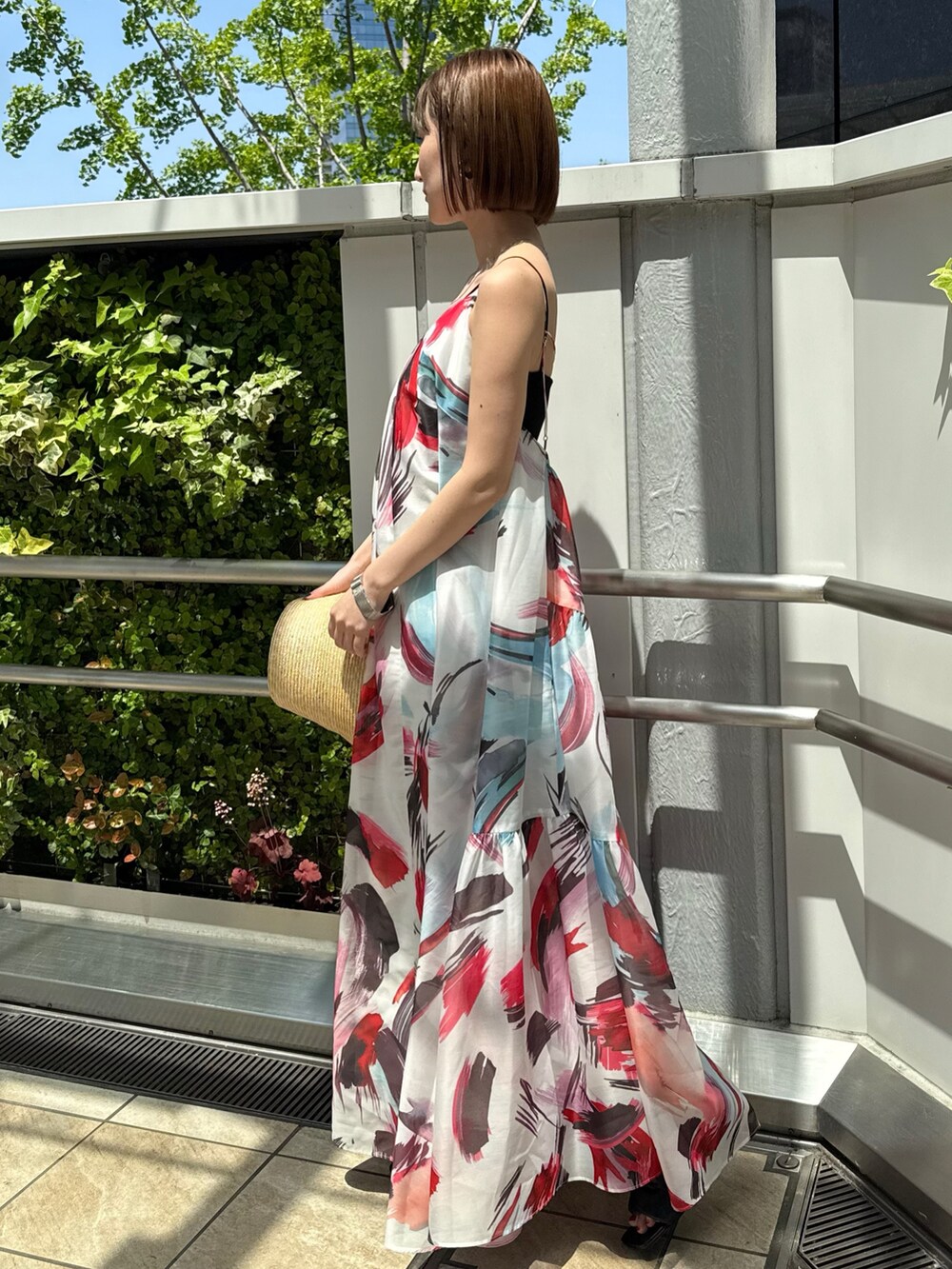 レッド系のワンピース、ブラック系のサンダル、ベージュ系のハットを着用したレディースの春コーディネートの3枚目の写真