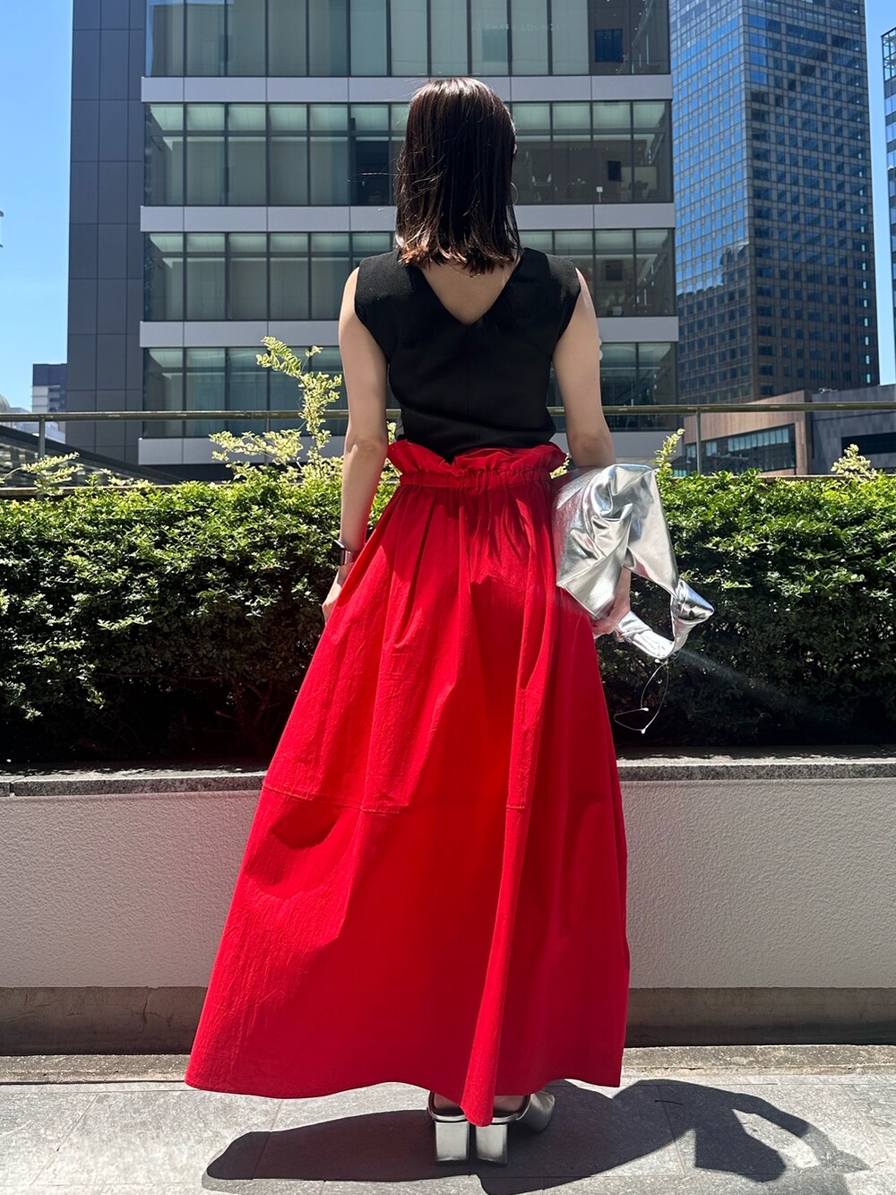 レッド系のスカート、シルバー系のトートバッグ、シルバー系のパンプスを着用したレディースの夏コーディネートの3枚目の写真