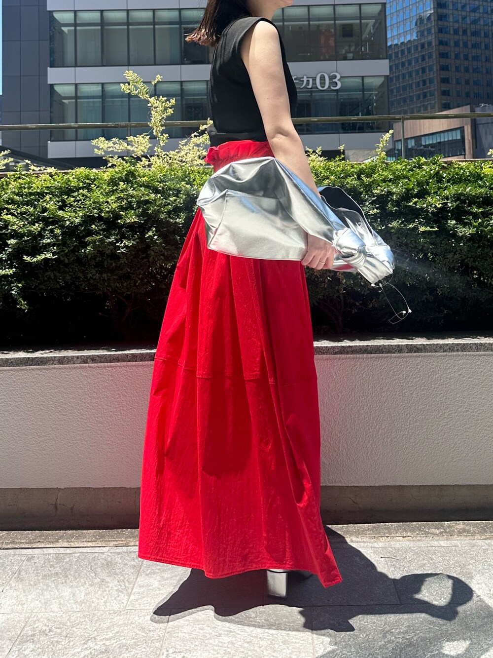 レッド系のスカート、シルバー系のトートバッグ、シルバー系のパンプスを着用したレディースの夏コーディネートの4枚目の写真