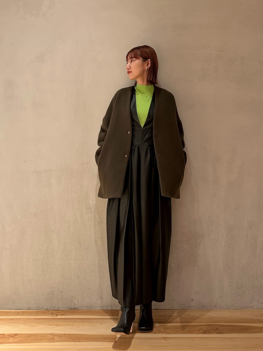 ブラック系のジャンパースカート、ブラック系のブーツ、グリーン系のニット/セーターを着用したレディースの秋コーディネートの2枚目の写真