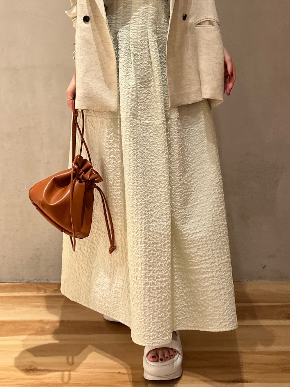 ベージュ系のテーラードジャケット、グリーン系のワンピース、ホワイト系のサンダルを着用したレディースの冬コーディネートの7枚目の写真