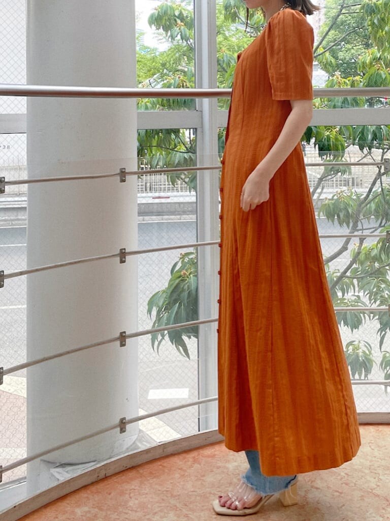 オレンジ系のワンピース、シルバー系のネックレスを着用したレディースの夏コーディネートの3枚目の写真