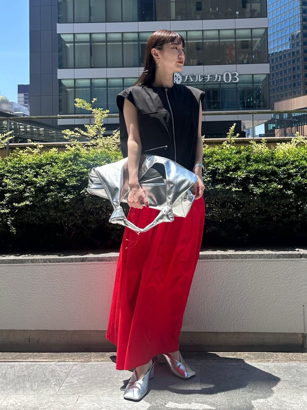 レッド系のスカート、シルバー系のパンプス、シルバー系のトートバッグを着用したレディースの夏コーディネートの2枚目の写真