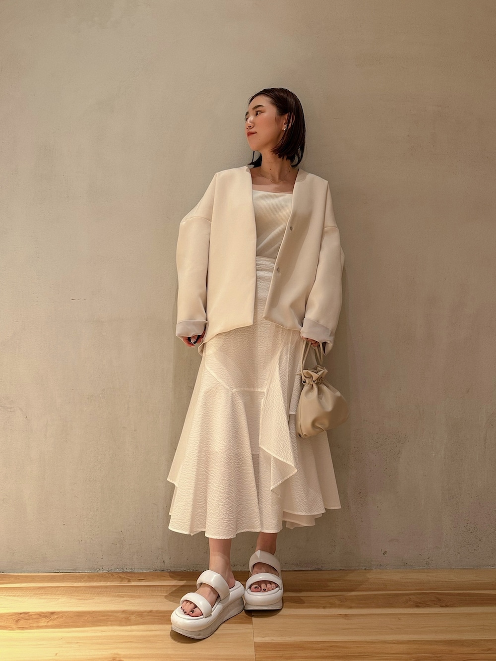 ブラウン系のノーカラーコート、ホワイト系のスカート、ホワイト系のサンダルを着用したレディースの春コーディネートの3枚目の写真
