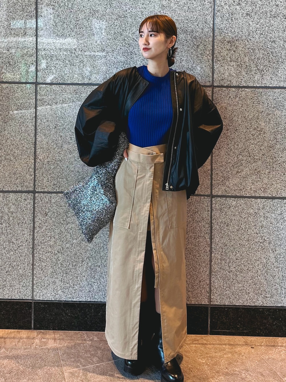 ブルー系のニット/セーター、ブラック系のノーカラージャケット、ベージュ系のスカートを着用したレディースの秋コーディネートの2枚目の写真