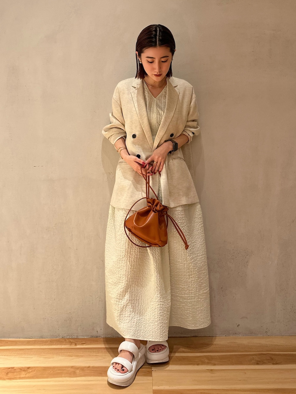 ベージュ系のテーラードジャケット、グリーン系のワンピース、ホワイト系のサンダルを着用したレディースの冬コーディネートの2枚目の写真