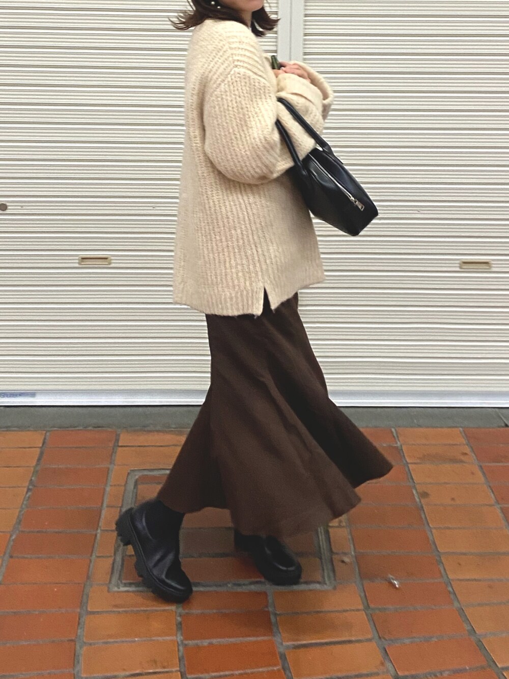 ブラック系のブーツ、ブラウン系のスカート、ベージュ系のニット/セーターを着用したレディースの秋コーディネートの2枚目の写真