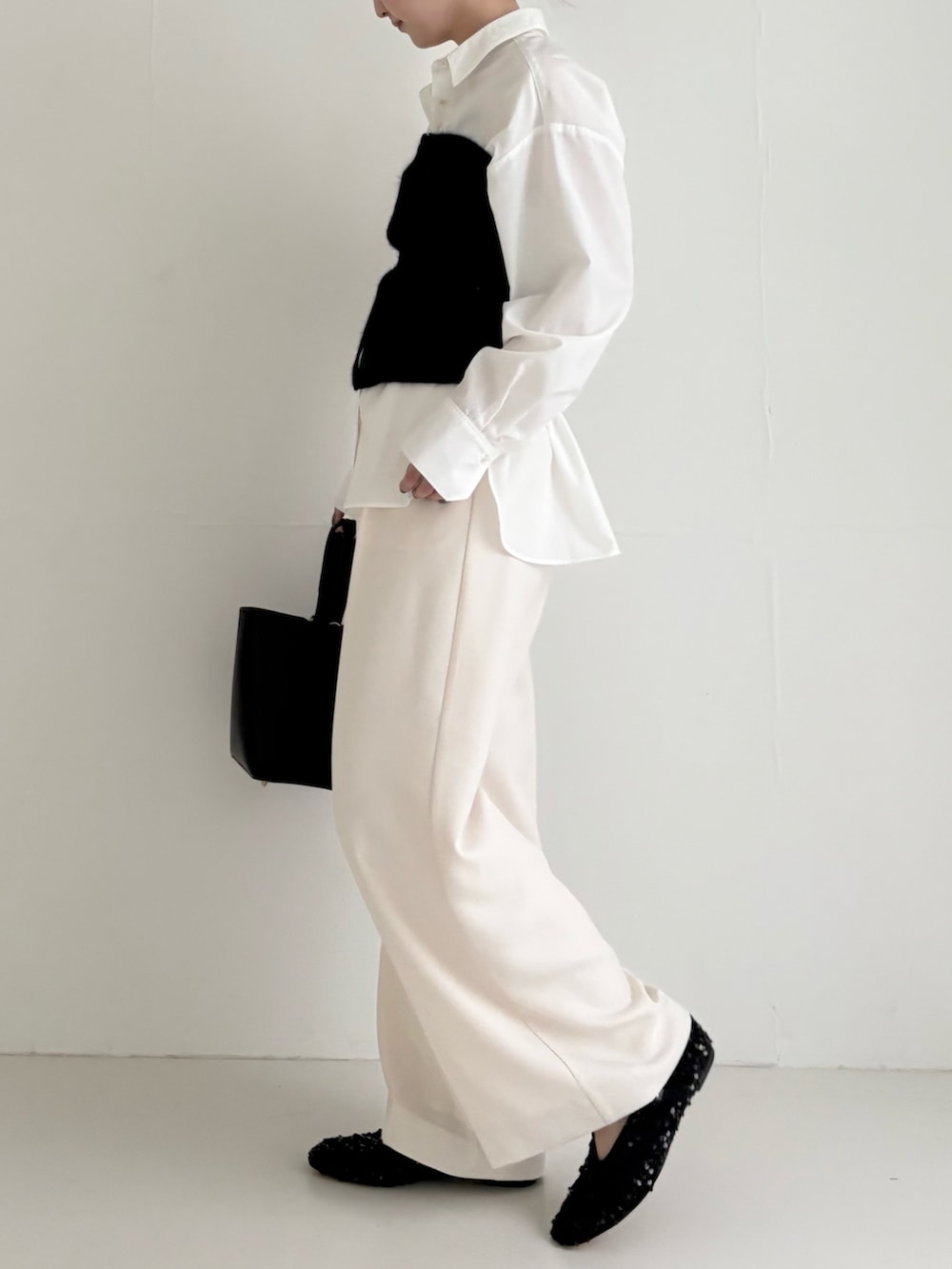 ブラック系のニット/セーター、ホワイト系のシャツ/ブラウス、ブラック系のハンドバッグを着用したレディースの秋コーディネートの2枚目の写真