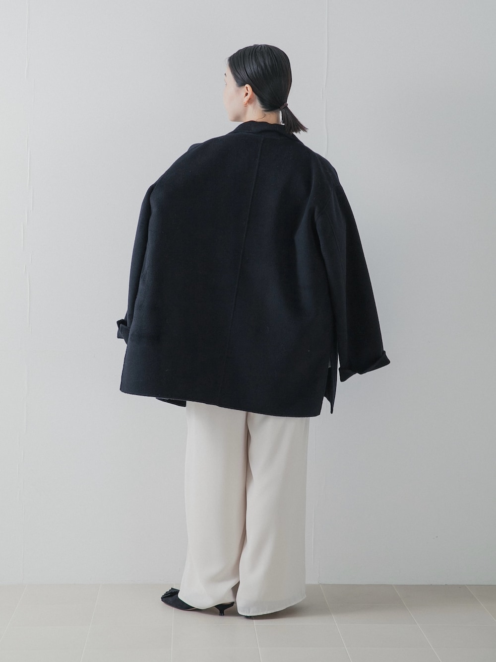 ブラック系のパンプス、ブラック系のチェスターコート、ホワイト系のその他パンツを着用したレディースの秋コーディネートの4枚目の写真