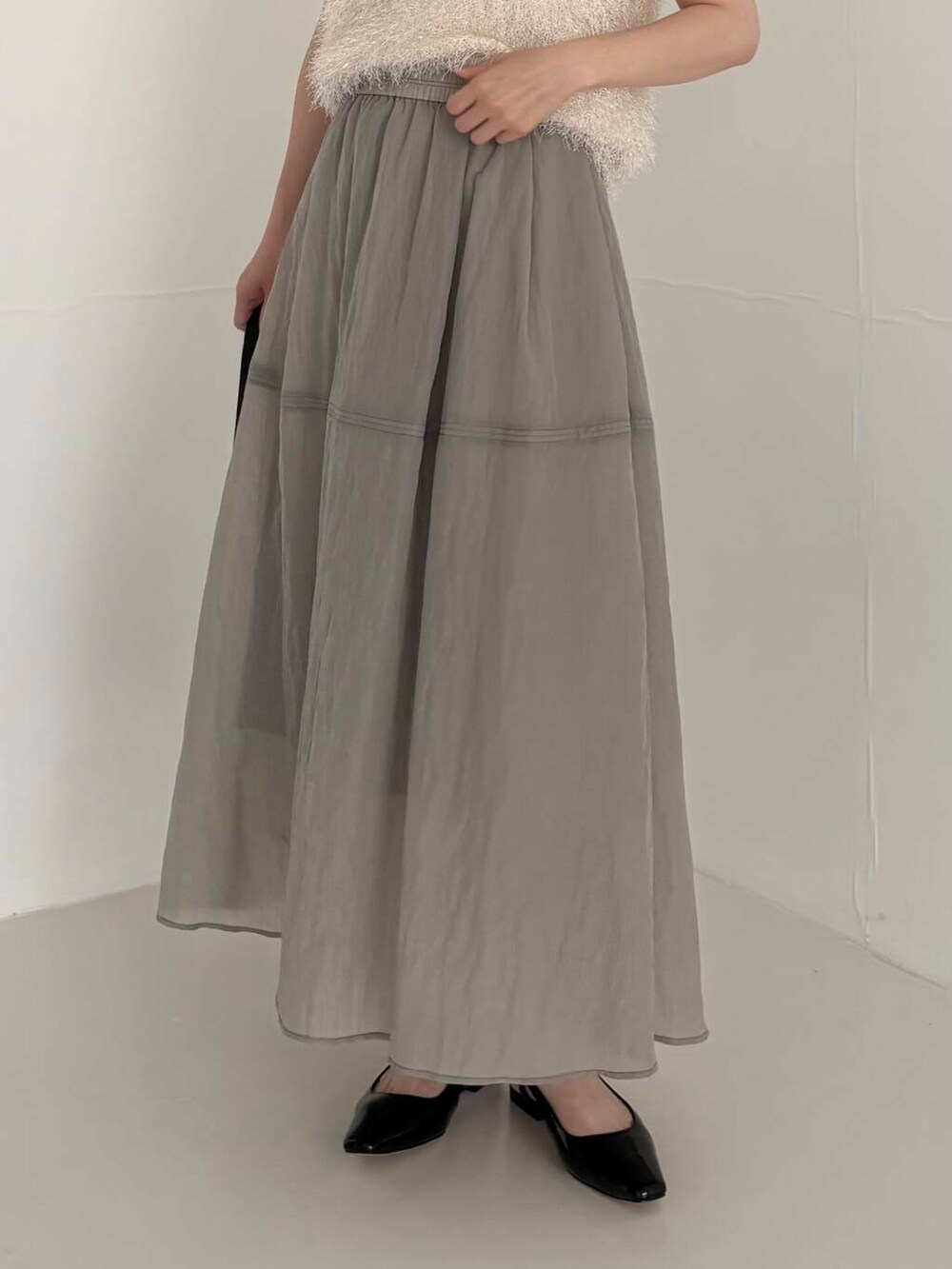 グレー系のスカート、ホワイト系のベスト、ブラック系のショルダーバッグを着用したレディースの夏コーディネートの3枚目の写真