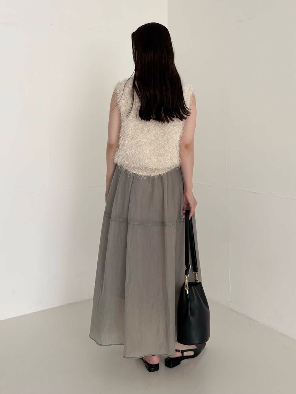 グレー系のスカート、ホワイト系のベスト、ブラック系のショルダーバッグを着用したレディースの夏コーディネートの2枚目の写真