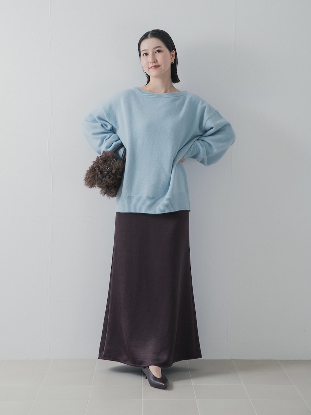 ブルー系のニット/セーター、ブラウン系のパンプス、ブラウン系のハンドバッグを着用したレディースの秋コーディネートの2枚目の写真