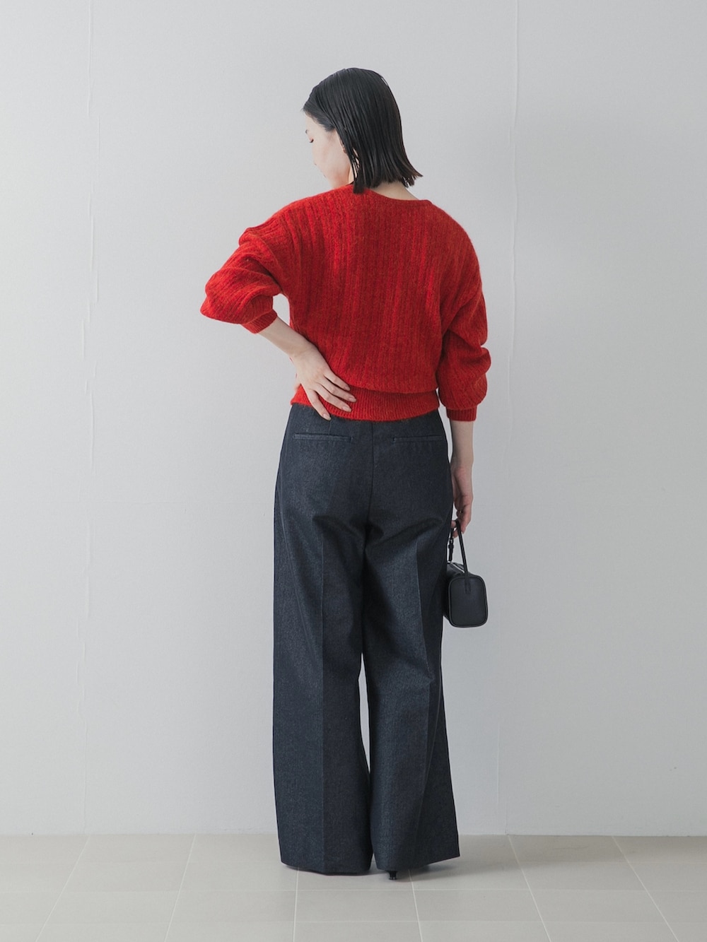レッド系のニット/セーター、ブルー系のデニムパンツ、ブラック系のハンドバッグを着用したレディースの秋コーディネートの4枚目の写真