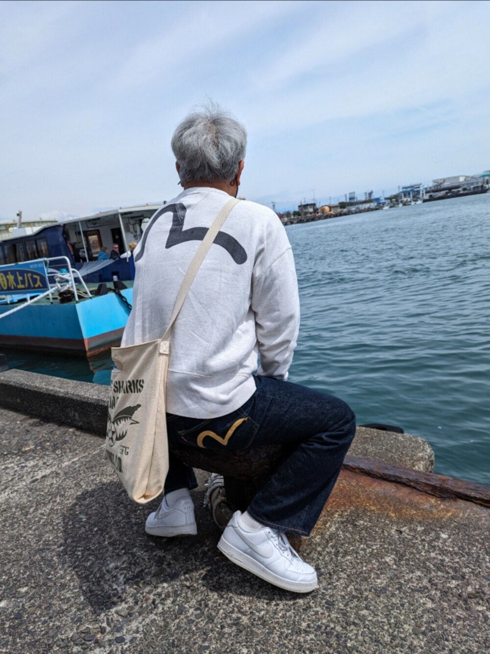 ホワイト系のスウェット、ベージュ系のショルダーバッグ、ブルー系のデニムパンツを着用したメンズの春コーディネートの2枚目の写真