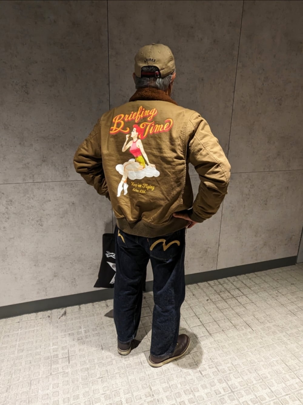 ベージュ系のミリタリージャケット、ホワイト系のスウェット、ブルー系のデニムパンツを着用したメンズの冬コーディネートの2枚目の写真