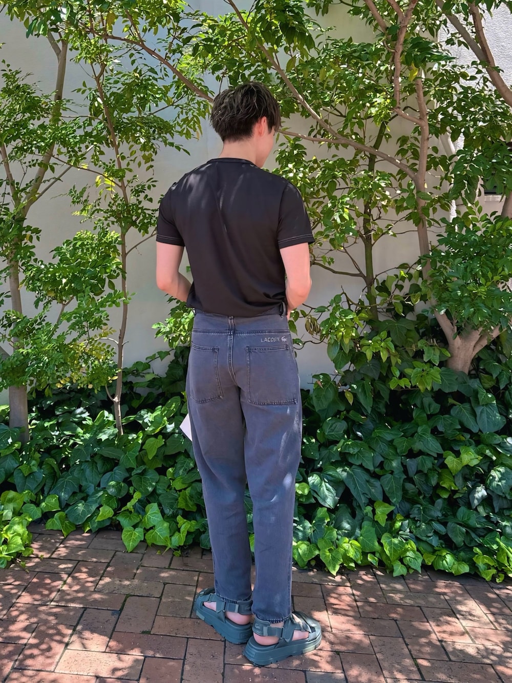 ブラック系のTシャツ/カットソー、ブラック系のデニムパンツ、ブラック系のクラッチバッグを着用したメンズの夏コーディネートの4枚目の写真