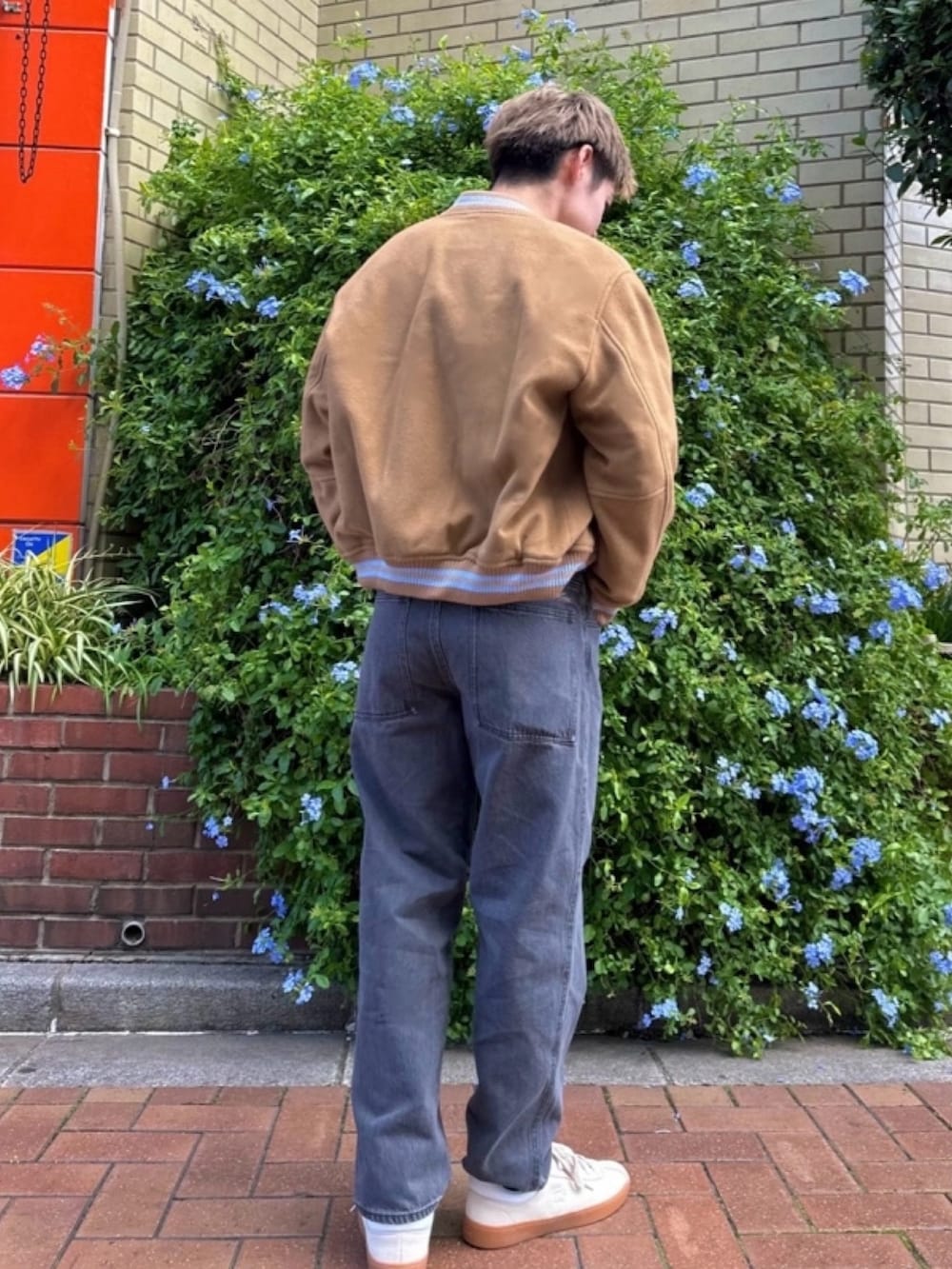 ブラウン系のブルゾン、ブルー系のニット/セーター、ブラック系のデニムパンツを着用したメンズの春コーディネートの2枚目の写真