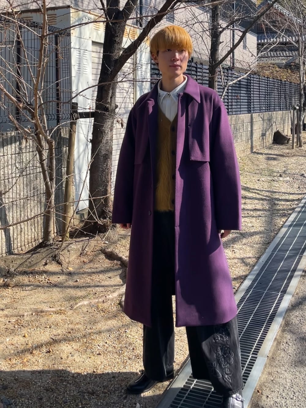 パープル系のステンカラーコート、ブラック系のデニムパンツ、ブラック系のドレスシューズを着用したメンズの冬コーディネートの2枚目の写真