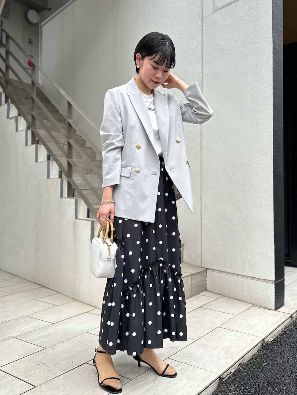 グレー系のテーラードジャケット、ホワイト系のTシャツ/カットソー、ブラック系のスカートを着用したレディースの春コーディネートの2枚目の写真