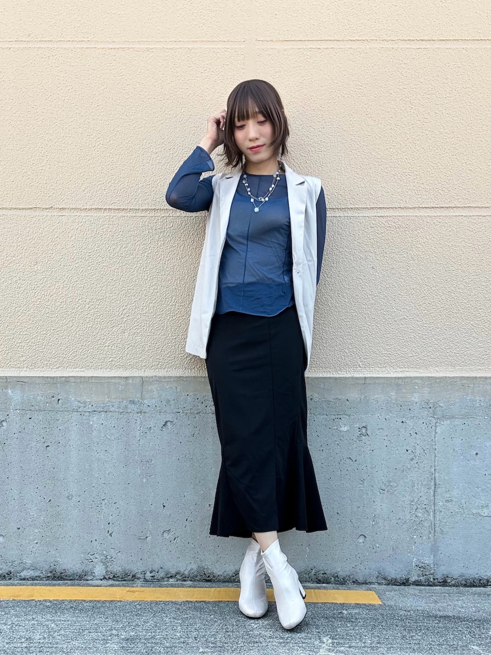 ブラック系のスカート、ホワイト系のベスト、ブルー系のトップスを着用したレディースの春コーディネートの2枚目の写真