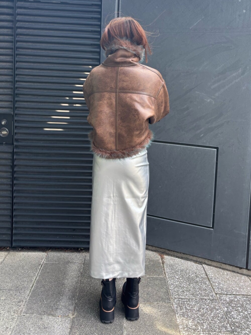 シルバー系のスカート、ブラック系のブーツ、ブラウン系のムートンコートを着用したレディースの夏コーディネートの3枚目の写真