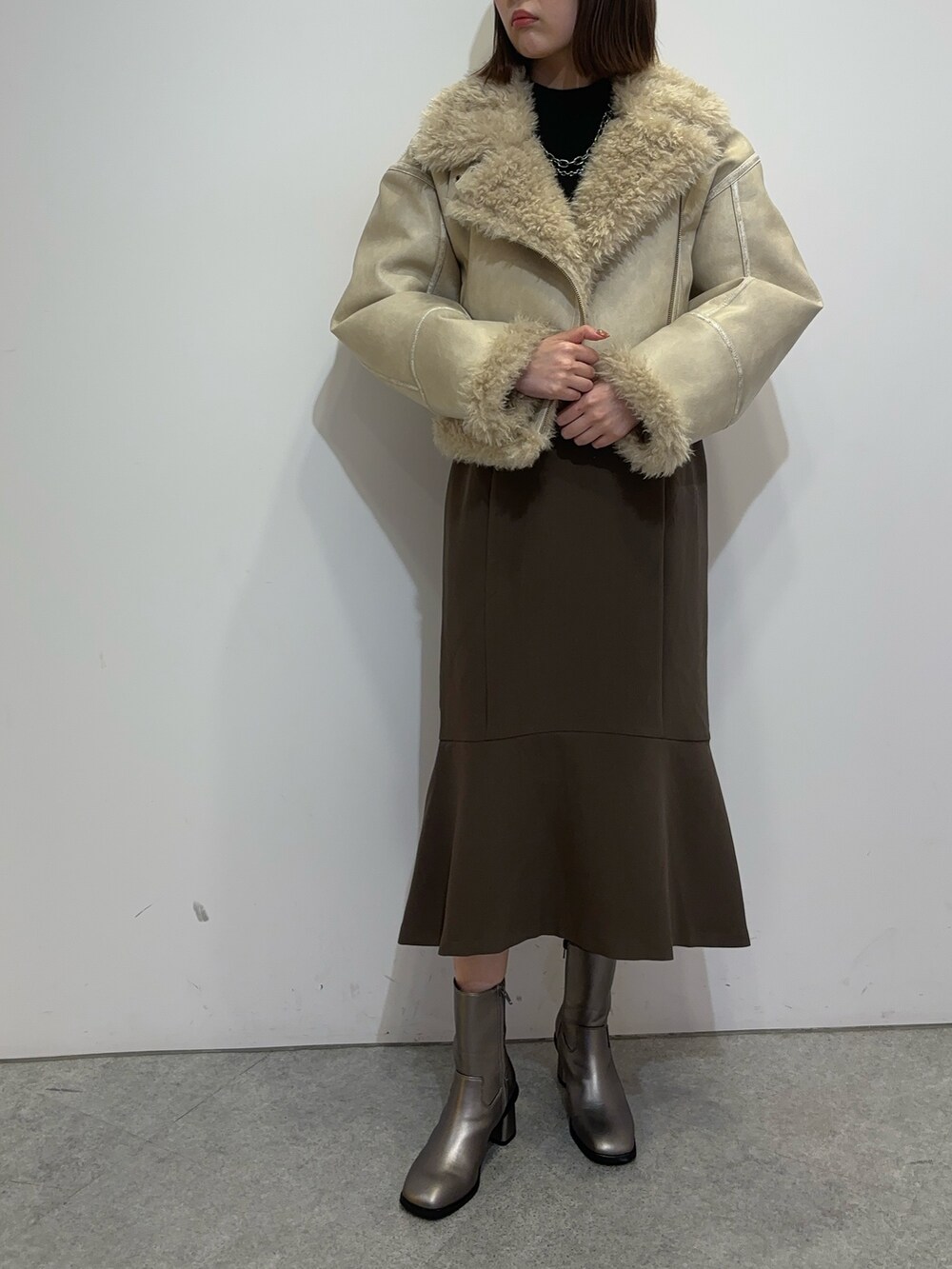 ブラウン系のスカート、ホワイト系のムートンコート、ブラウン系のブーツを着用したレディースの夏コーディネートの2枚目の写真