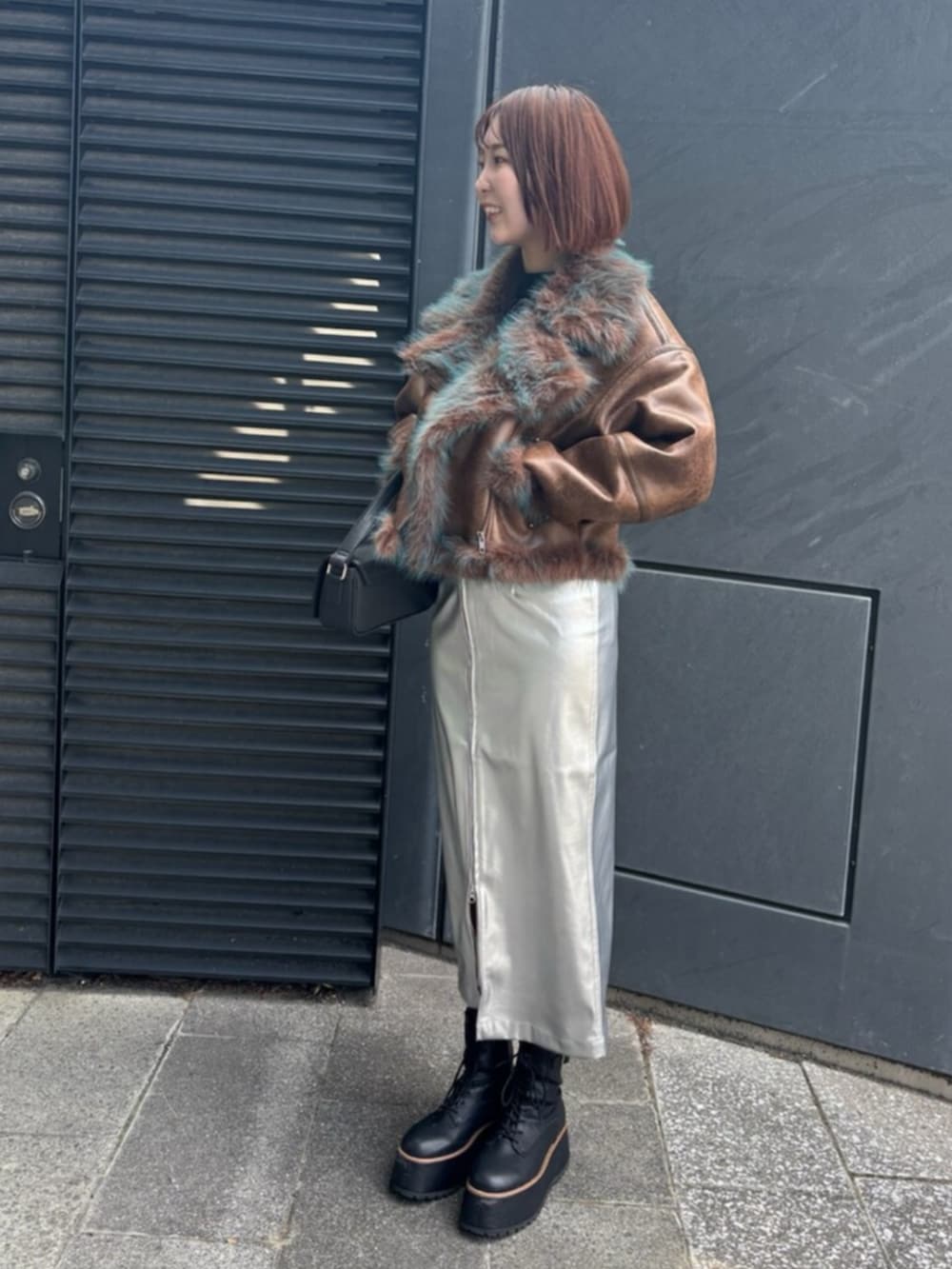 シルバー系のスカート、ブラック系のブーツ、ブラウン系のムートンコートを着用したレディースの夏コーディネートの2枚目の写真