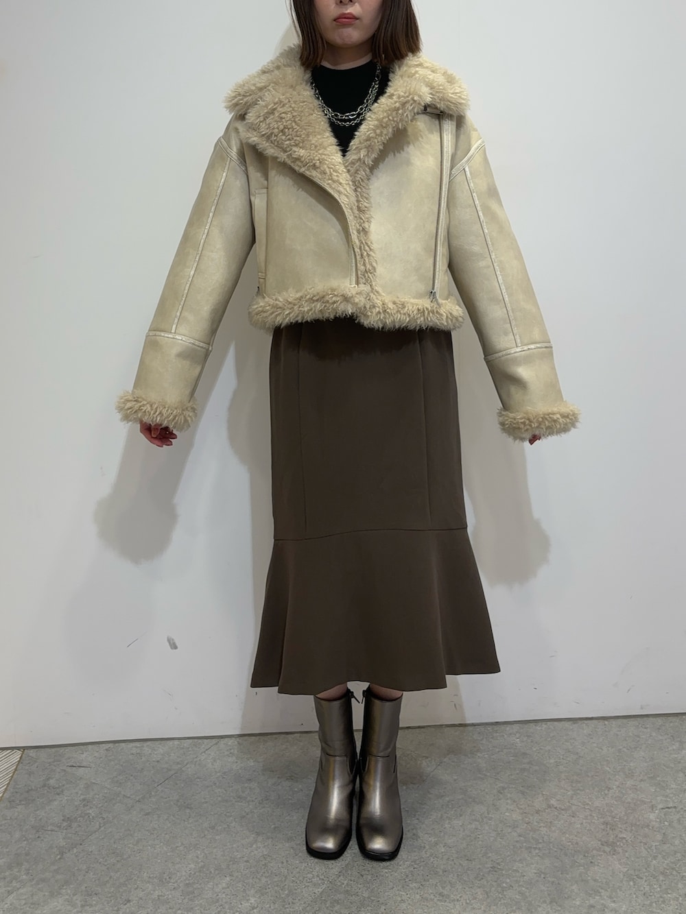 ブラウン系のスカート、ホワイト系のムートンコート、ブラウン系のブーツを着用したレディースの夏コーディネートの3枚目の写真