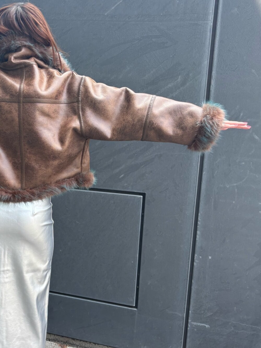 シルバー系のスカート、ブラック系のブーツ、ブラウン系のムートンコートを着用したレディースの夏コーディネートの5枚目の写真