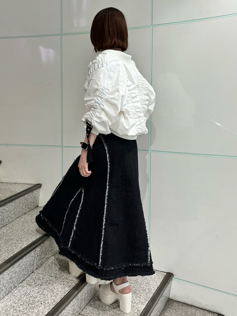 ブラック系のデニムスカート、ホワイト系のブルゾン、ホワイト系のサンダルを着用したレディースの春コーディネートの2枚目の写真