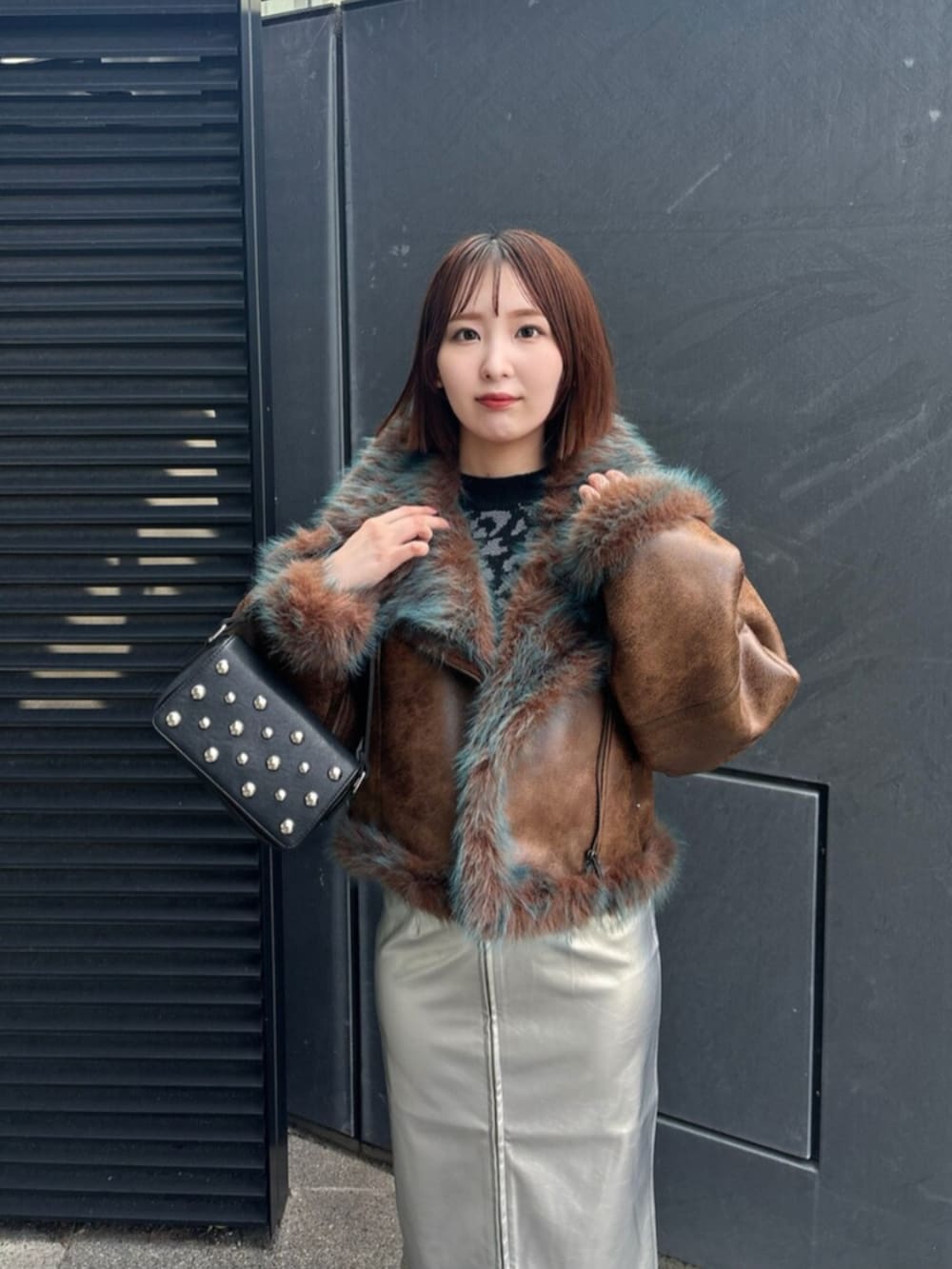 シルバー系のスカート、ブラック系のブーツ、ブラウン系のムートンコートを着用したレディースの夏コーディネートの4枚目の写真