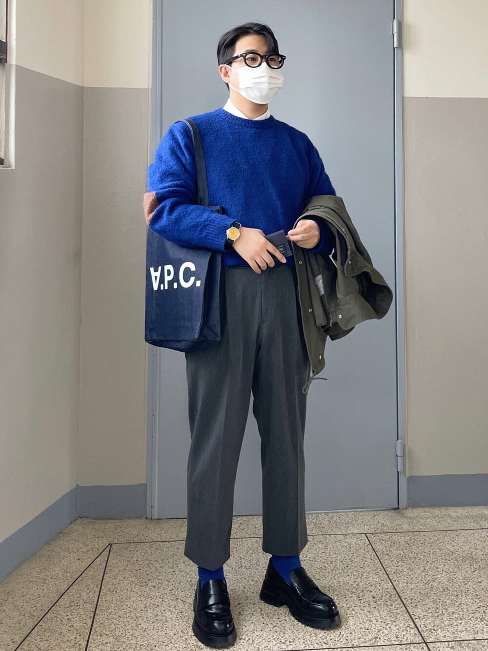 ブルー系のニット/セーター、ブルー系のトートバッグ、グリーン系のミリタリージャケットを着用したメンズの春コーディネートの2枚目の写真