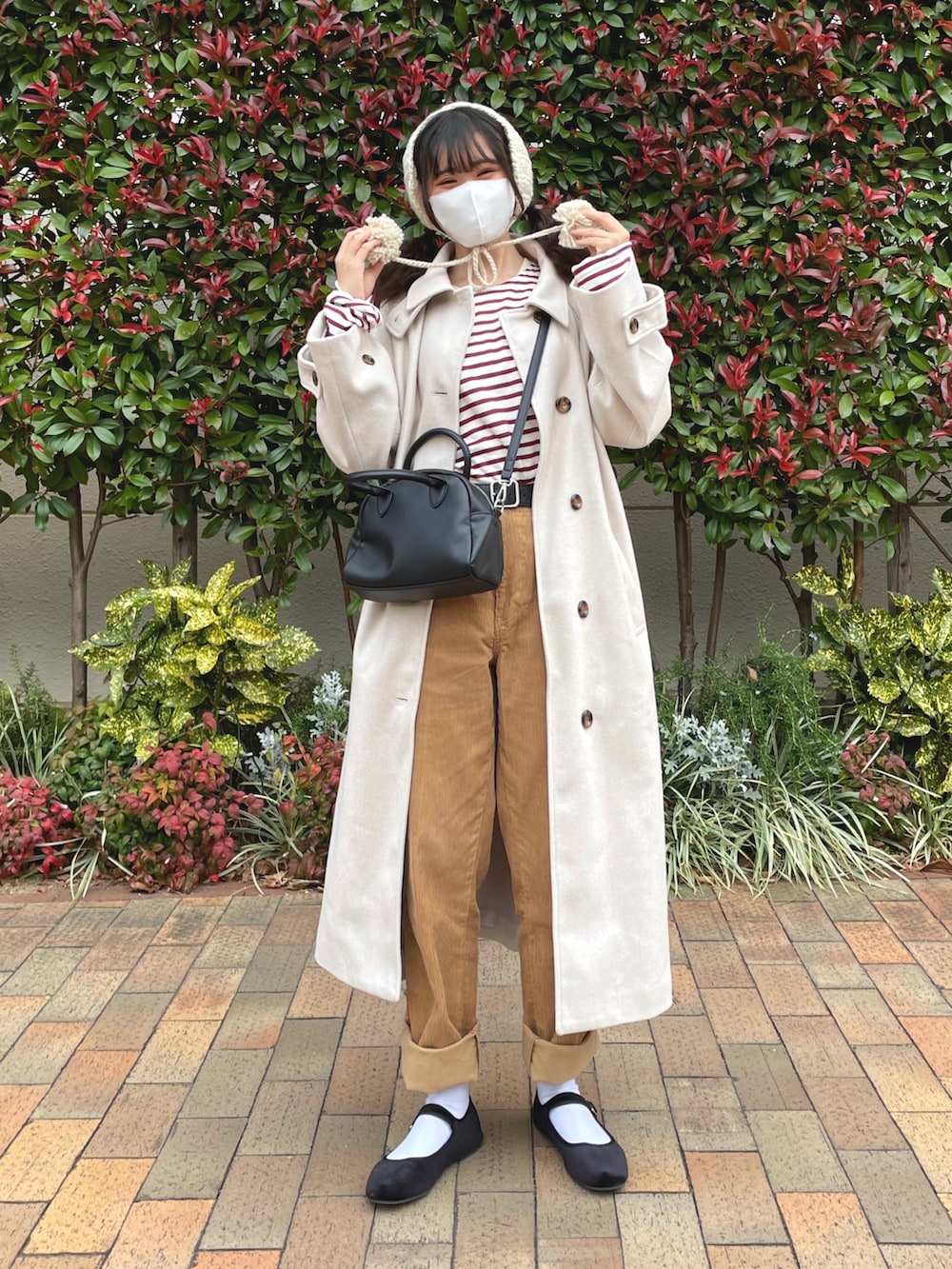 ホワイト系のステンカラーコート、レッド系のTシャツ/カットソー、ブラック系のボストンバッグを着用したレディースの冬コーディネートの2枚目の写真