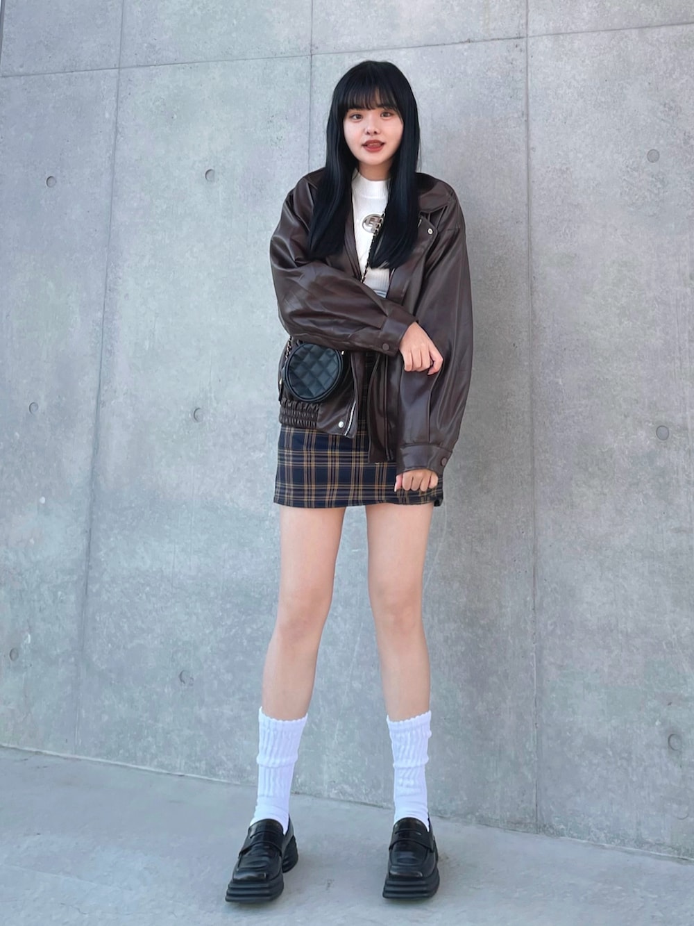 ブラウン系のライダースジャケット、ホワイト系のニット/セーター、ブルー系のスカートを着用したレディースの冬コーディネートの2枚目の写真