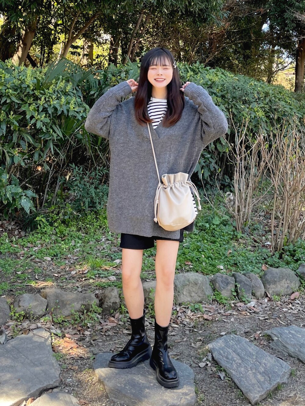 グレー系のニット/セーター、ブラック系のTシャツ/カットソー、ブラウン系のショルダーバッグを着用したレディースの春コーディネートの2枚目の写真