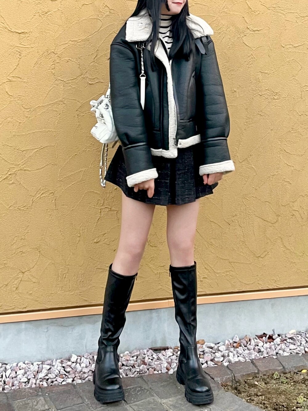 ブラック系のムートンコート、ホワイト系のニット/セーター、ブラック系のスカートを着用したレディースの冬コーディネートの3枚目の写真