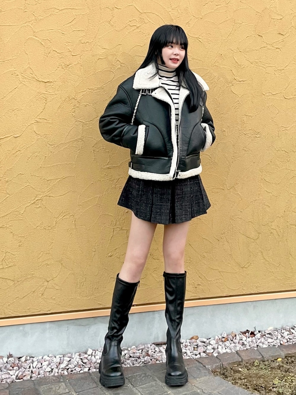 ブラック系のムートンコート、ホワイト系のニット/セーター、ブラック系のスカートを着用したレディースの冬コーディネートの2枚目の写真