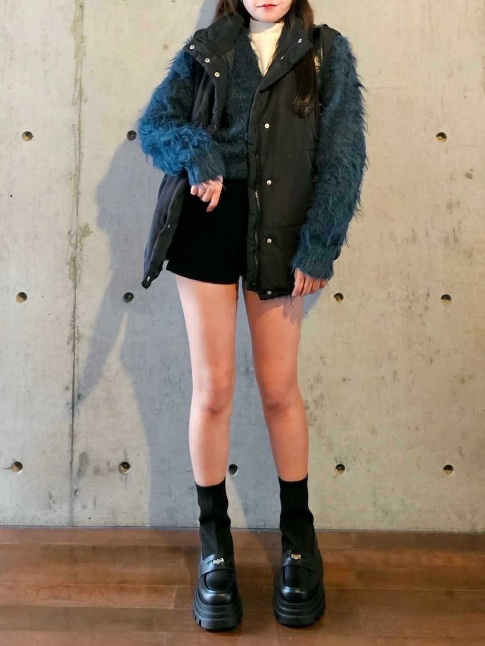 ブラック系のブーツ、ブルー系のカーディガン/ボレロ、ブラック系のダウンベストを着用したレディースの秋コーディネートの3枚目の写真