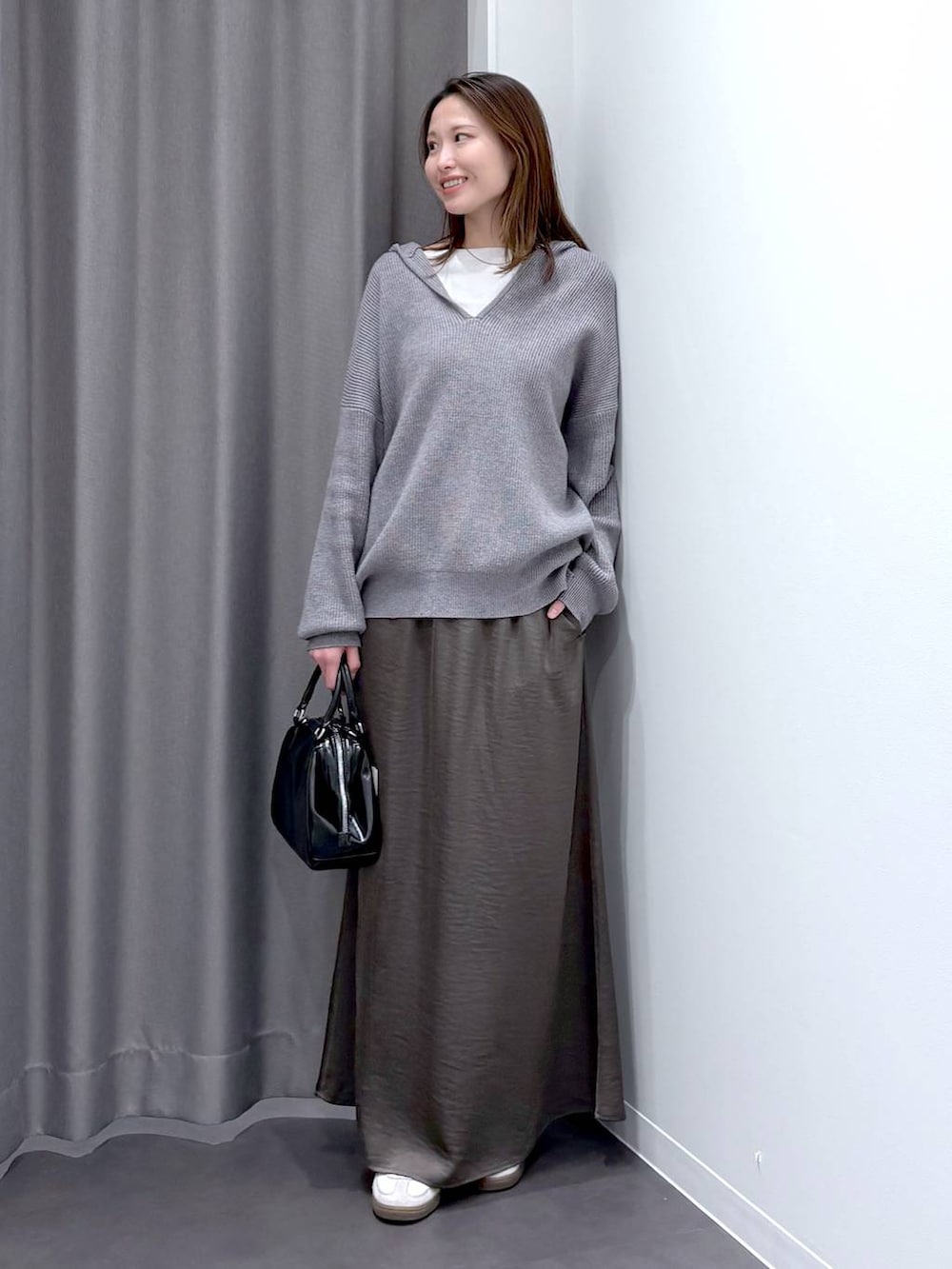 グレー系のスカート、グレー系のニット/セーター、ブラック系のショルダーバッグを着用したレディースの秋コーディネートの2枚目の写真