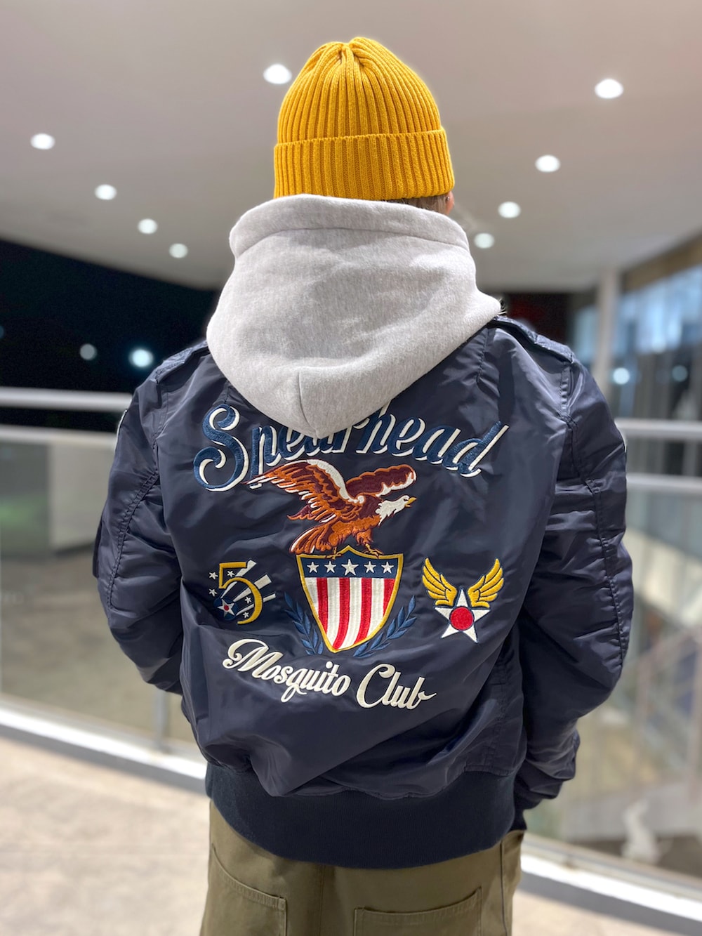 グリーン系のサロペット/オーバーオール、ブルー系のミリタリージャケット、イエロー系のニットキャップ/ビーニーを着用したレディースの秋コーディネートの2枚目の写真