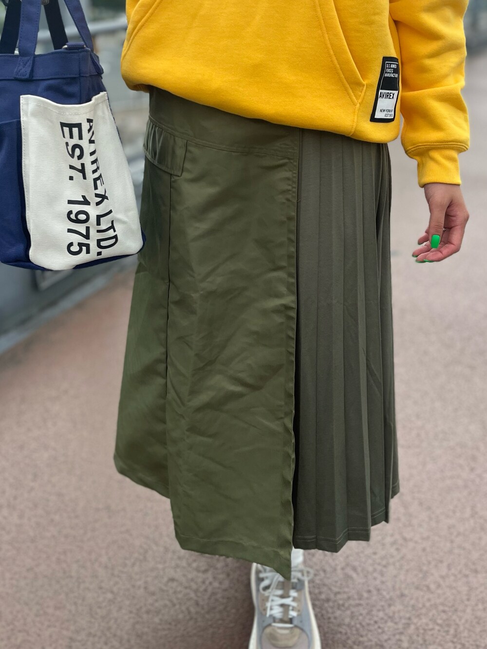 イエロー系のパーカー、ブルー系のトートバッグ、グリーン系のスカートを着用したレディースの秋コーディネートの3枚目の写真